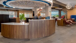 Ein Hotel-Rezeptionsbereich mit einem Holzbüro, einem digitalen Bildschirm und einer Sitzecke mit Stühlen.