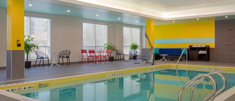 An indoor swimming pool with clear lane markings, a seating area with chairs, and a small table.