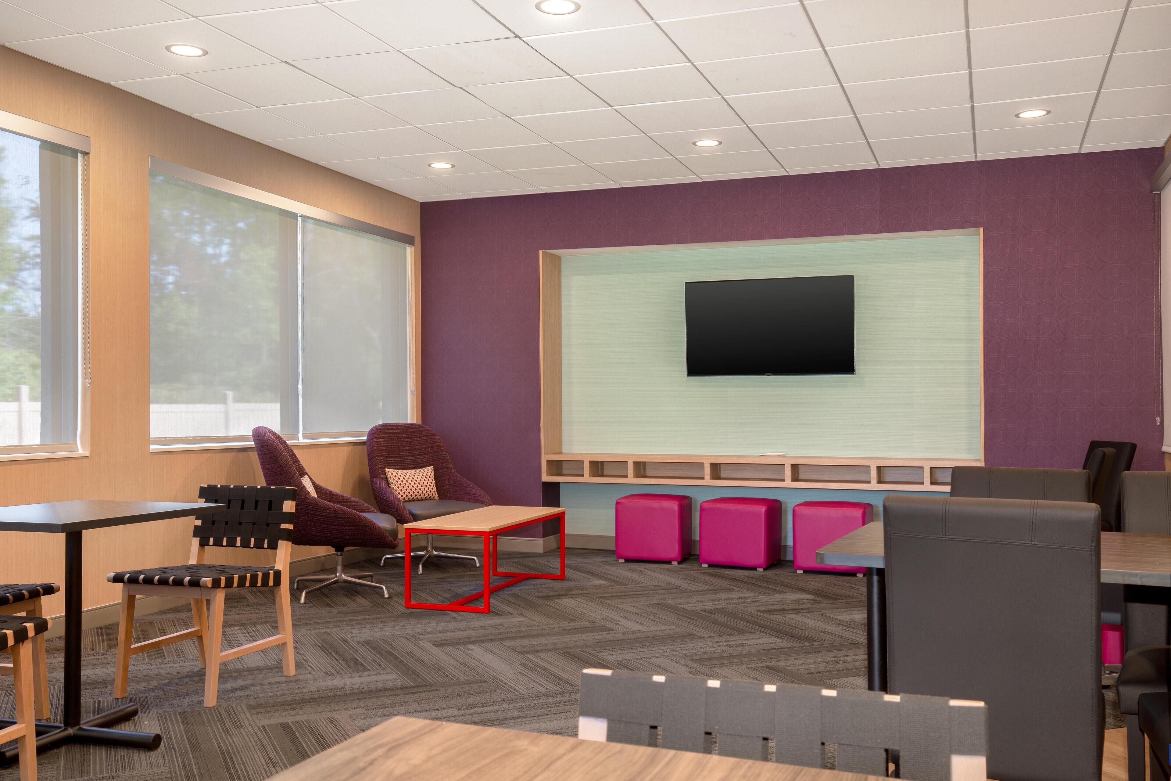 A modern office space with a large screen, comfortable seating, and a herringbone-patterned carpet.