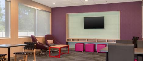 A modern office space with a large screen, comfortable seating, and a herringbone-patterned carpet.