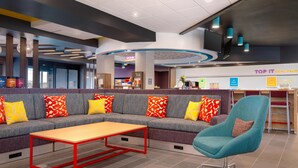 Eine moderne Lounge-Ecke mit einem grauen Ecksofa, einem Tisch mit rotem Rahmen und einem blaugrünen Sessel.