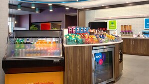 Ein Selbstbedienungsbereich mit Getränken und Snacks, darunter eine Kühlvitrine sowie eine Auswahl an Joghurt und Käse.