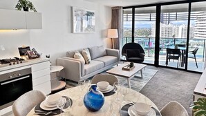 A modern hotel room with a dining area, a sofa, a coffee table, and a view of the cityscape. - Perfect beach pad Oracle Tower 2 Lvl 8 Parking (Broadbeach)