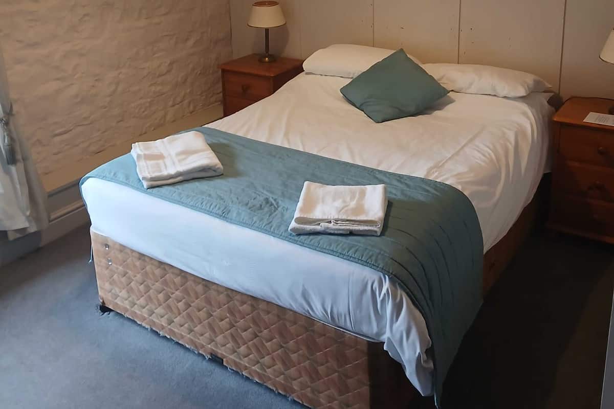 A neatly made bed with a quilted headboard, a bedside lamp, and a folded towel on the bed.