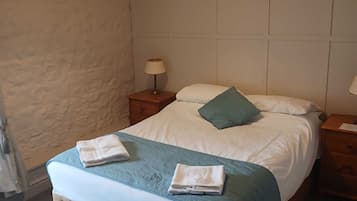 Un lit bien fait, avec une tête de lit matelassée, une lampe de chevet et une serviette pliée posée sur le lit.