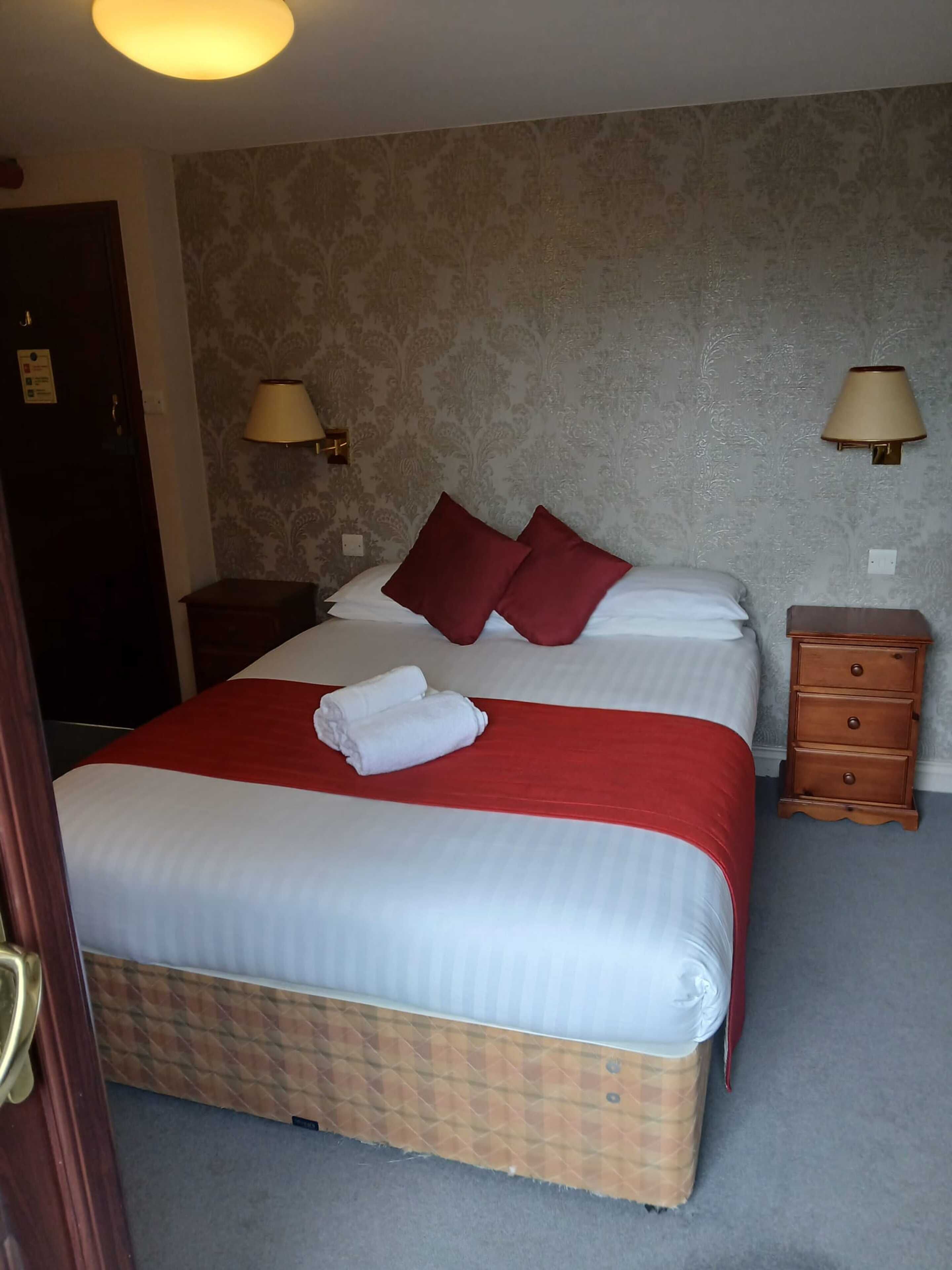 A hotel room with a bed, two bedside lamps, a wooden nightstand, and a door.