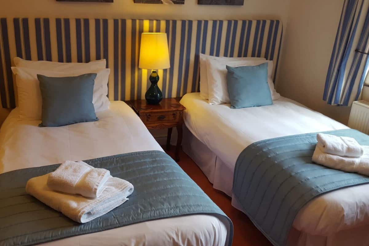 A hotel room with two beds, striped headboards, a bedside lamp, and neatly folded towels on each bed.