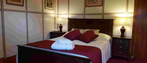 A neatly made bed with a red bedspread and pillows, flanked by two bedside tables with lamps, in a room with framed artwork on the walls.