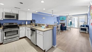 A modern kitchen with stainless steel appliances, a central island, and a dining area with a blue chair. - OCbeachparadise, Paradise Off The Boardwalk (Ocean City)