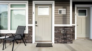 Un edificio de dos pisos con puertas numeradas, un muro de piedra decorativo y una silla de metal negro en el exterior.