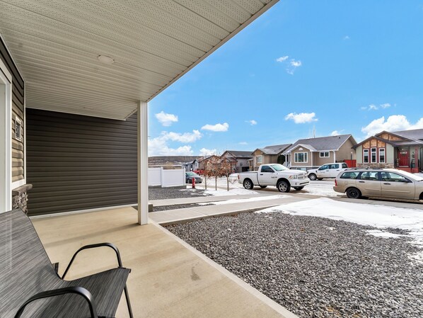 A covered outdoor area with a bench, a gravel path, and a view of residential houses and parked cars.