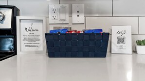 Una cocina moderna con azulejos blancos, un cartel de bienvenida, una cesta de artículos de aseo y el símbolo de WiFi.