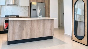 A modern kitchen with a marble countertop, a built-in stove, and a refrigerator. - Brand new apt w 2 Bedrooms Terrace in Cap Cana (Punta Cana)