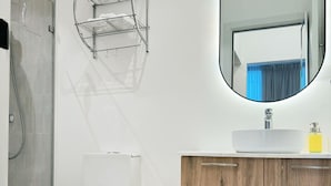 A modern bathroom with a white toilet, a wooden vanity, a mirror, and a towel rack. - Brand new apt w 2 Bedrooms Terrace in Cap Cana (Punta Cana)