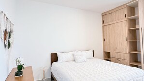 A bedroom with a bed, wooden wardrobe, and a small table with a plant. - Brand new apt w 2 Bedrooms Terrace in Cap Cana (Punta Cana)