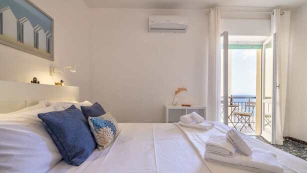 Habitación de hotel con cama, mesita de noche, espejo, aire acondicionado y vista al mar por una puerta abierta.