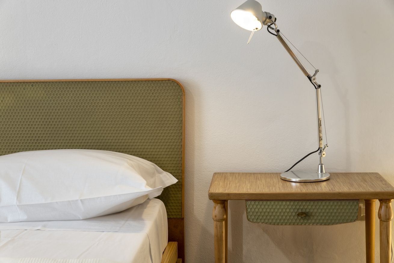 En seng med et grønt sengegavl, en hvid pude og et trænatbord med en lampe.