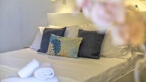 Una cama bien hecha con almohadas, una lámpara fijada a la pared y un enchufe visible.