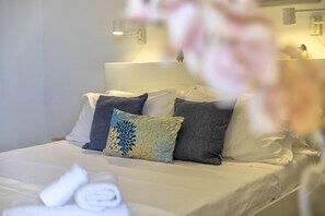 Una cama bien hecha con almohadas, una lámpara fijada a la pared y un enchufe visible.