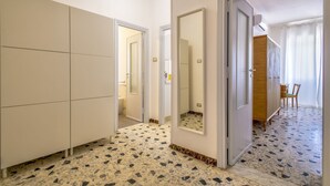 Una habitación con suelo de baldosas, un armario, un espejo y una puerta que da a otra estancia.
