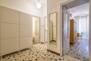 Una habitación con suelo de baldosas, un armario, un espejo y una puerta que da a otra estancia.