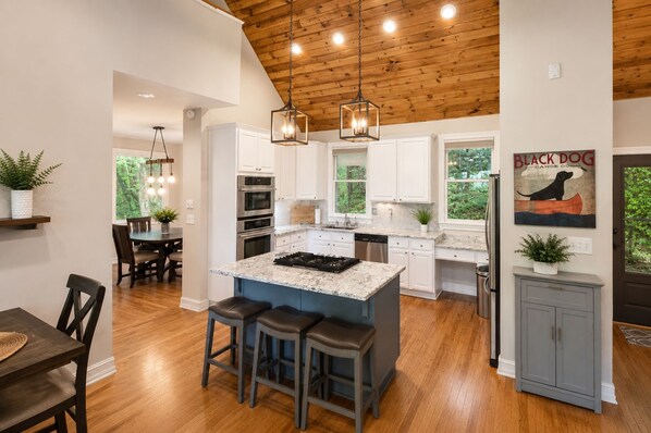 A modern kitchen with a central island, wooden ceiling, and pendant lighting.