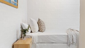 Un dormitorio ordenado con cama, almohadas, una mesita de noche con una planta y una colcha.