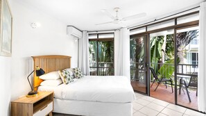 Ein Schlafzimmer mit einem Bett, einem Nachttisch, einem Deckenventilator und Blick ins Freie durch eine Glastür.