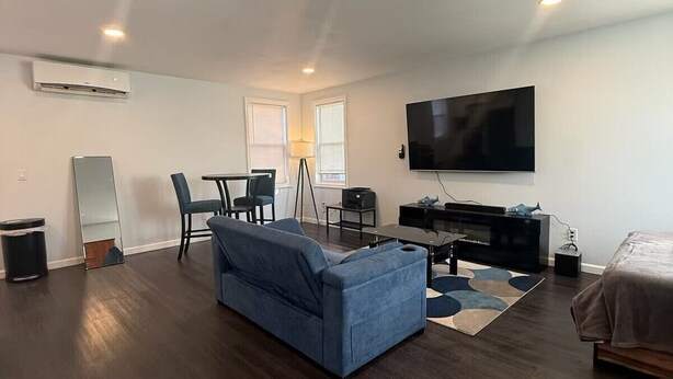 A modern living room with a blue sofa, a flat-screen TV, a coffee table, and a bed. - Lucy Private Studio (Providence)