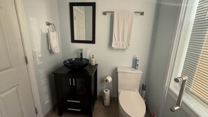A bathroom with a black vanity, a white toilet, a mirror, and a window with blinds. - Lucy Private Studio (Providence)