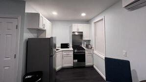 A compact kitchen with white cabinets, a refrigerator, a microwave, a stove, and a trash bin. - Lucy Private Studio (Providence)