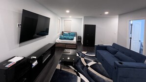 A modern living room with a flat-screen TV, a sofa, a bed, and a desk with a printer. - Lucy Private Studio (Providence)
