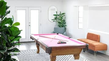 A modern room with a pool table, a potted plant, a chair, and a sofa.