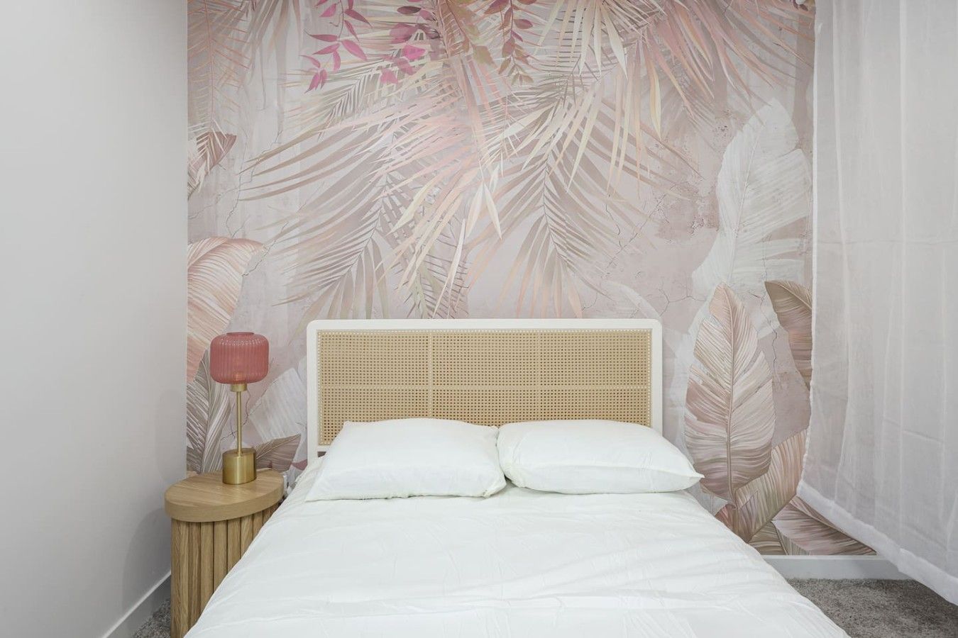 A bed with a woven headboard, white bedding, and a wall with a tropical leaf pattern.