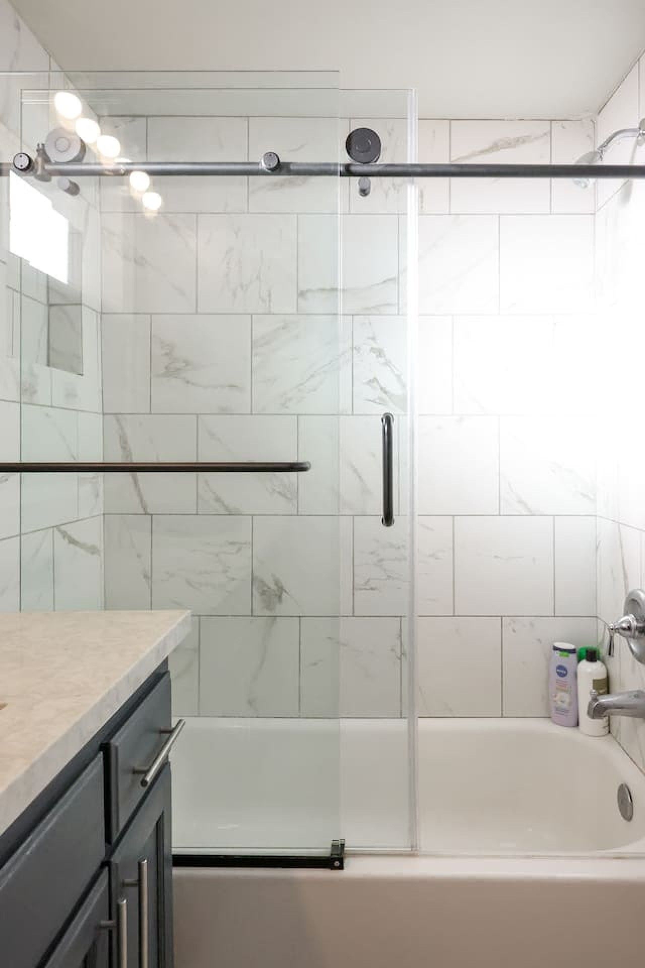 A modern bathroom with a glass shower enclosure, a bathtub, and a marble-tiled wall.