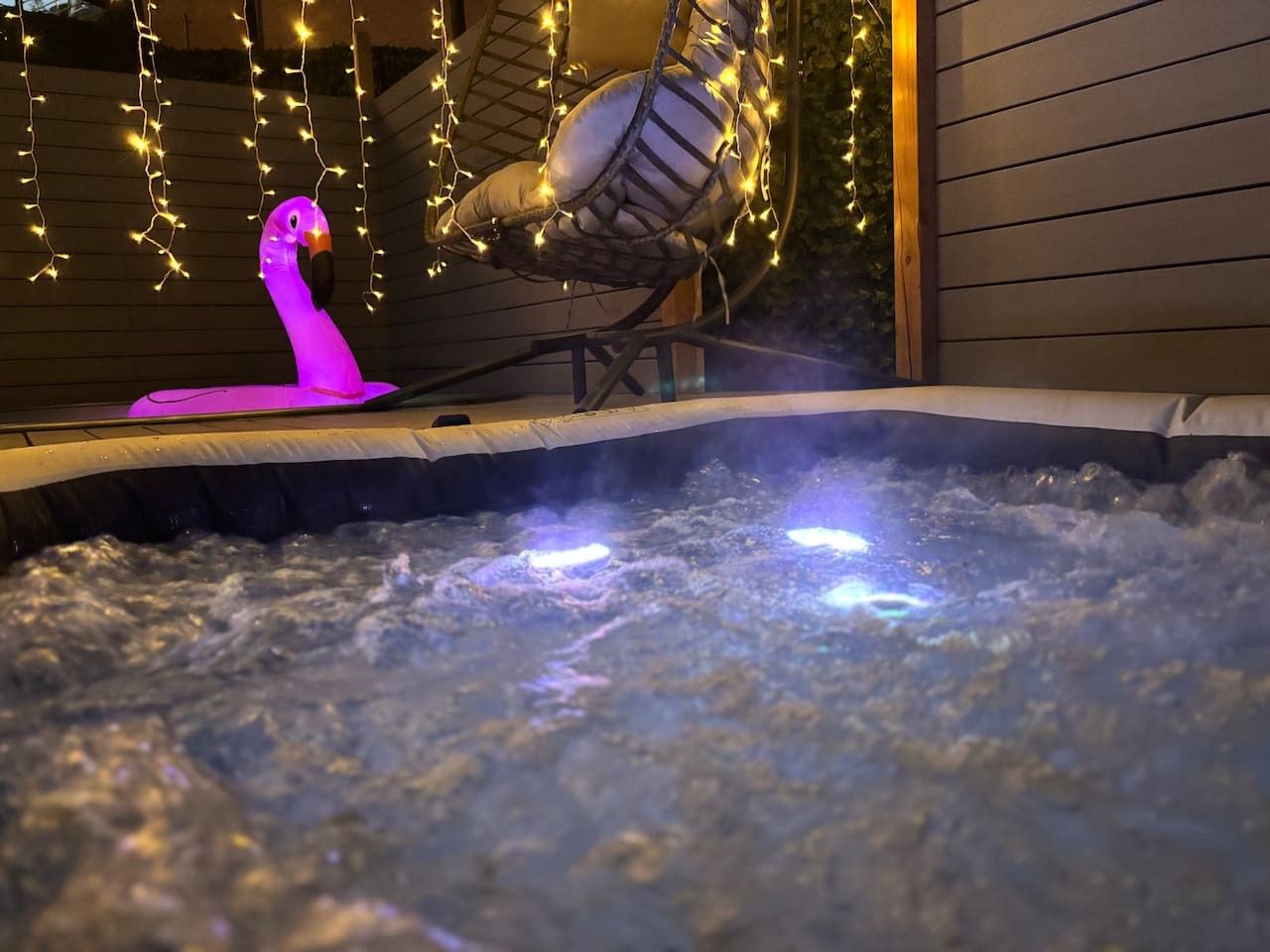 A hot tub with a pink flamingo decoration and a hanging chair with string lights.
