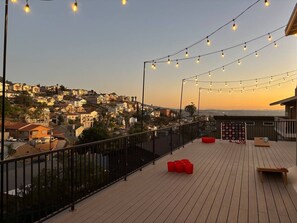 A rooftop terrace with a view of a residential area, string lights, and outdoor seating.