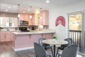 A modern kitchen with pink cabinets, a central island, and a dining area with chairs.