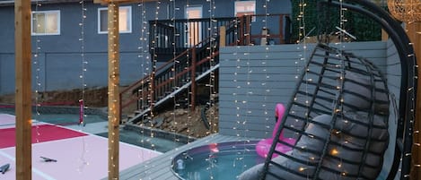 A wooden deck with a hot tub, a pink flamingo chair, and string lights.
