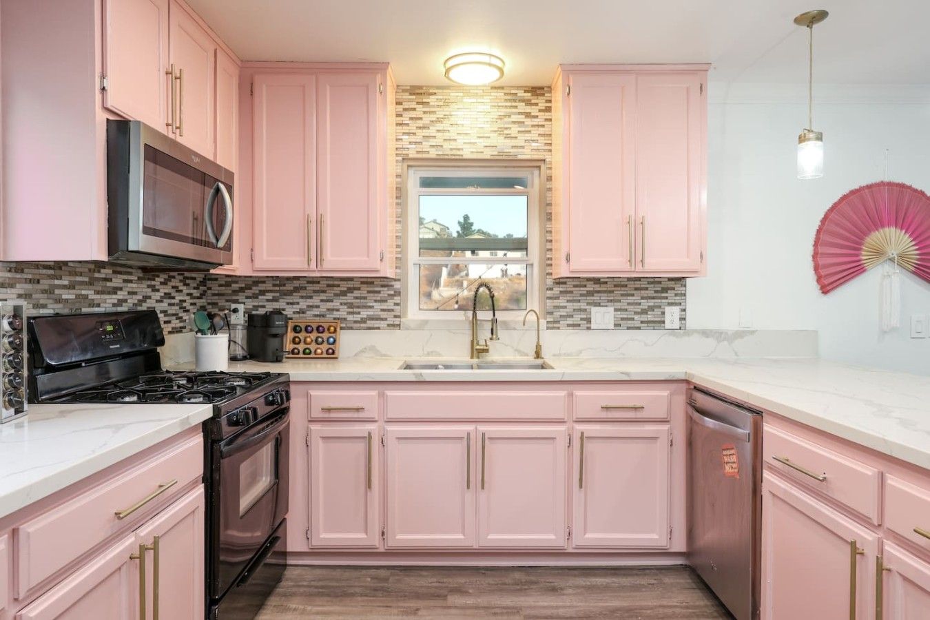 Una cocina con gabinetes rosas, un microondas, una estufa y un lavamanos.