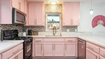 Una cocina con gabinetes rosas, un microondas, una estufa y un lavamanos.