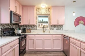A kitchen with pink cabinets, a microwave, a stove, and a sink.