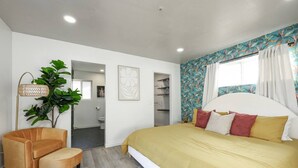 A bedroom with a large bed, a chair, a plant, and a bathroom visible through an open door. - SD Lux Oasis: Theatre, Spa, 14Beds, AC, Sleeps 20+ (Spring Valley)