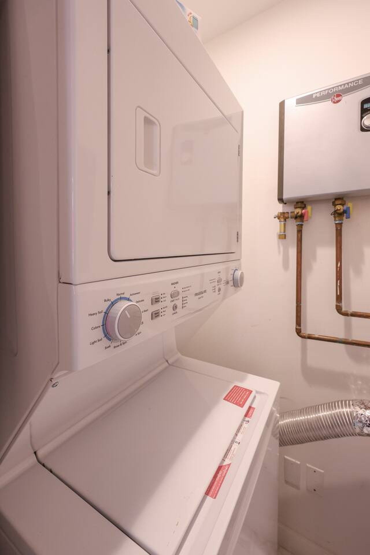 En hvid vaskemaskine med kontrolpanel, vandtilslutning og et ventilationsrør.