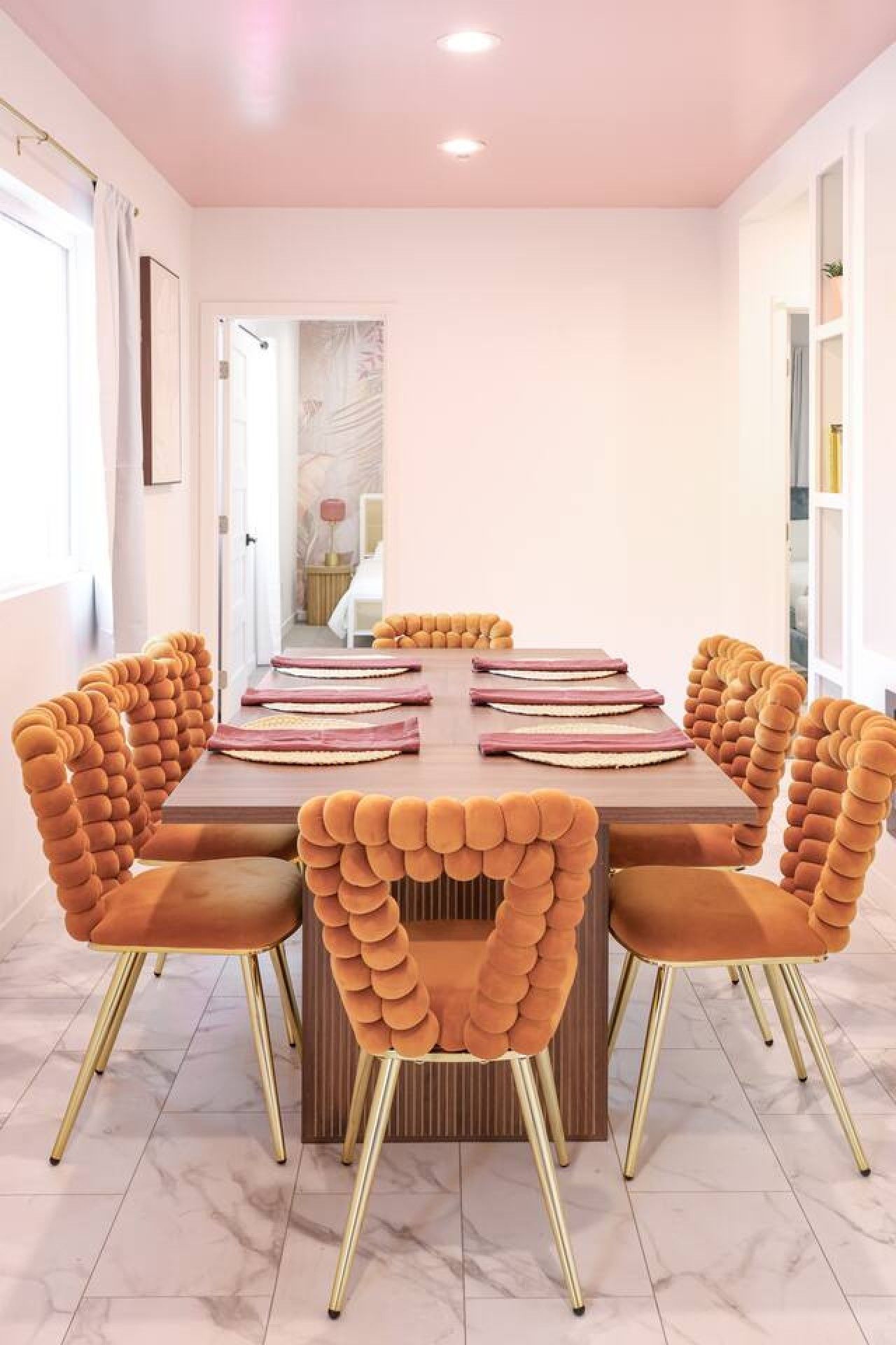 A dining area with a rectangular table, six upholstered chairs with a unique design, and a marble floor.