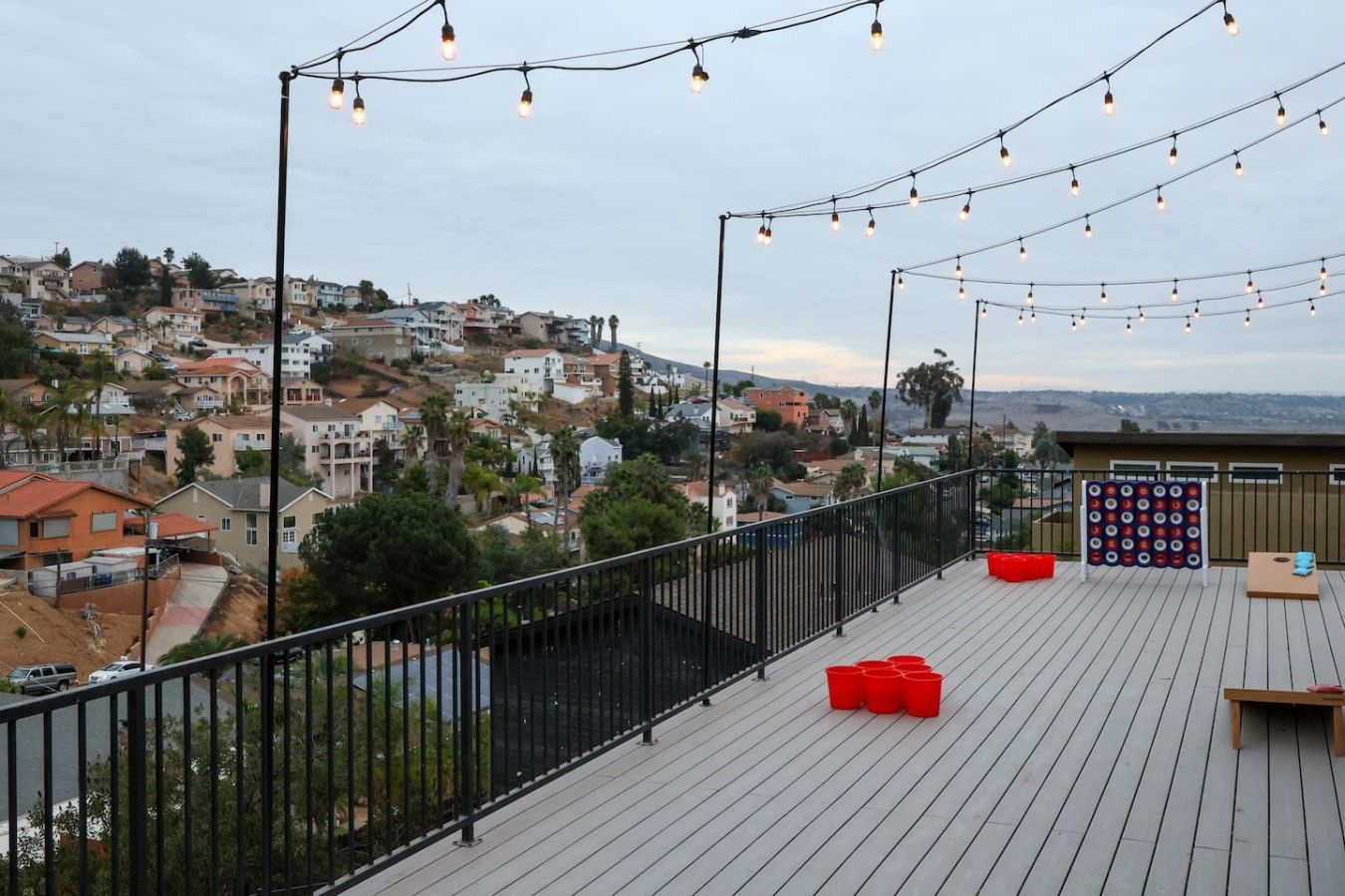 A rooftop terrace with string lights, a dartboard, and red chairs.