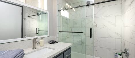 A modern bathroom with a glass shower enclosure, a vanity with a mirror, and a bathtub.