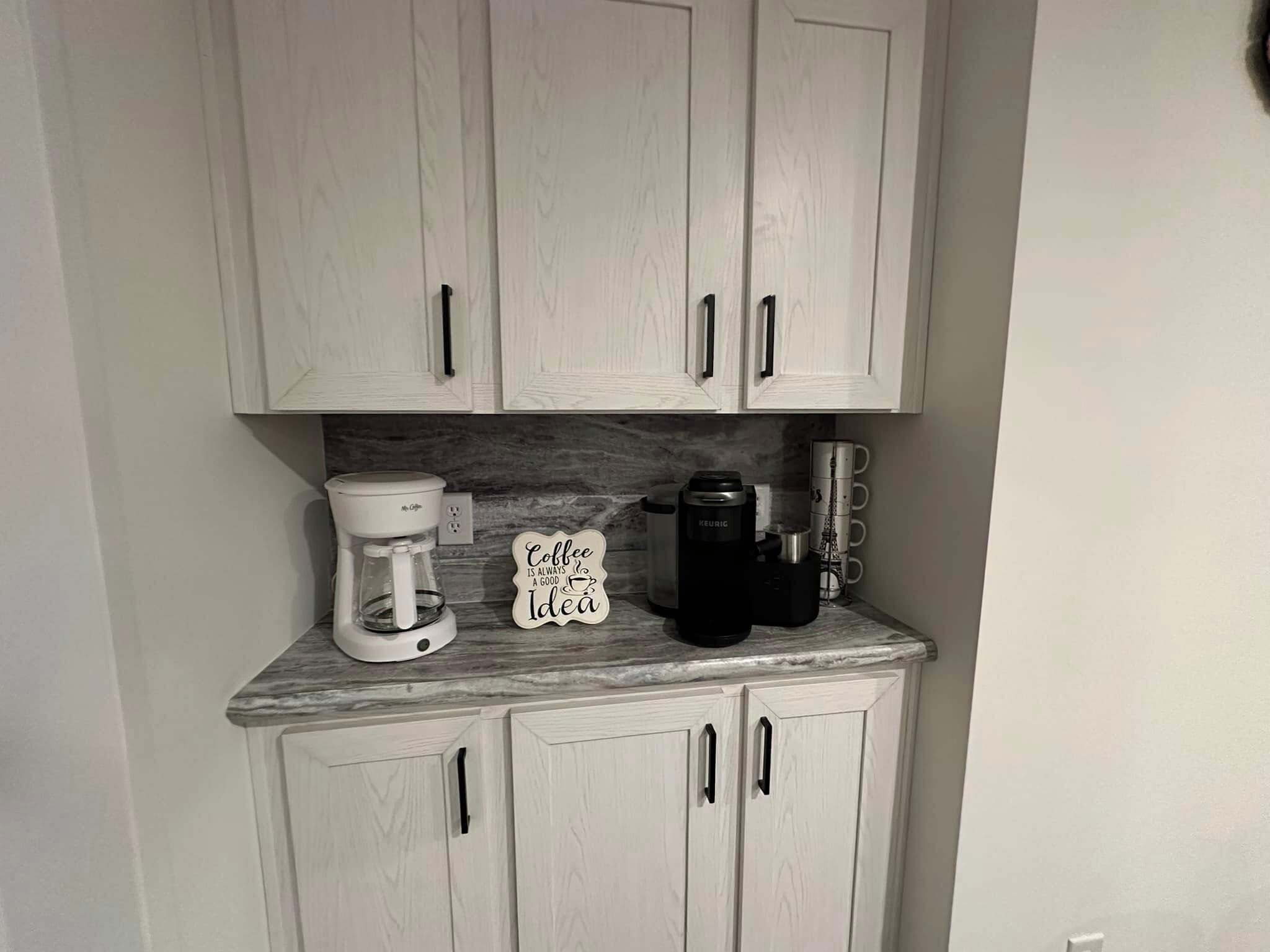 Een keuken met witte kastjes, een koffiezetapparaat, een Keurig, en een bordje met de tekst 'Koffie is altijd een goed idee'.
