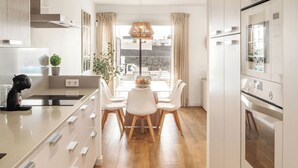 Een moderne keuken met witte kasten, een houten vloer en een eethoek met witte stoelen en een tafel.