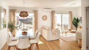 Een moderne woonkamer met een glazen eettafel, witte banken en een groot raam.